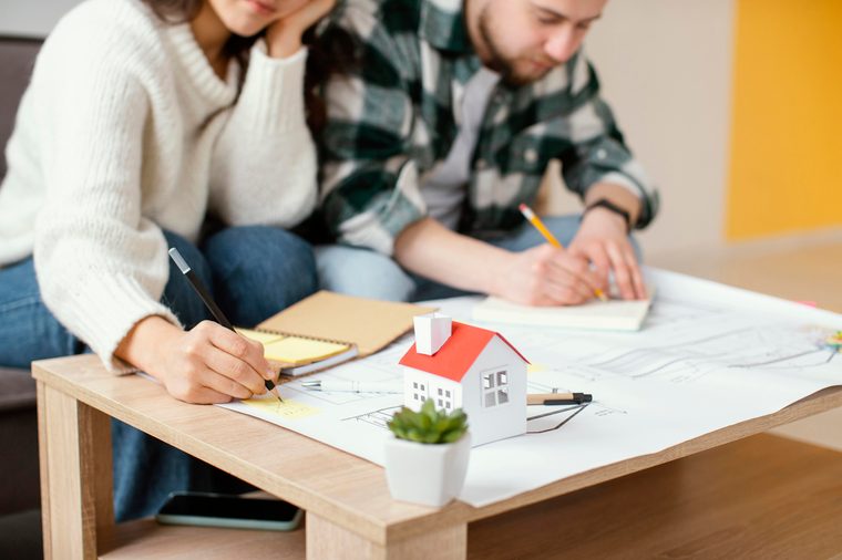 Um casal toma notas sobre as plantas da casa, com uma maqueta na mesa
